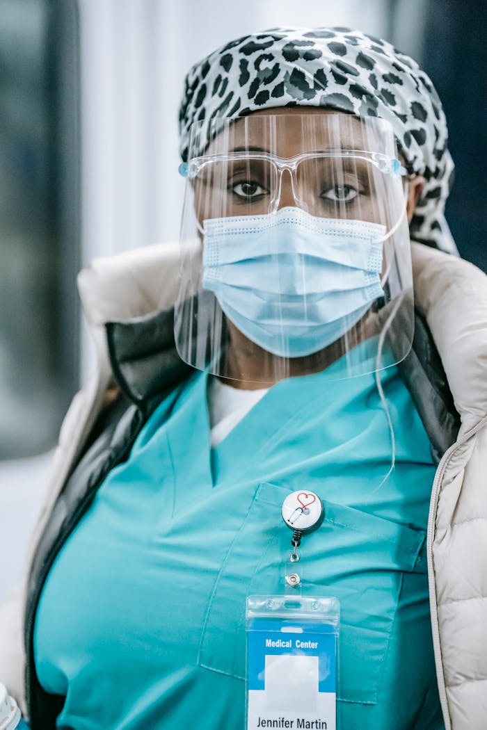Serious African American female medic in sterile mask and glasses standing in hospital and looking at camera